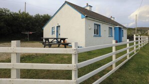 Een wit huis met blauwe accenten en een klein terras met een tafel en stoelen.