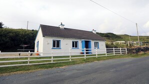 Een wit huis met blauwe accenten en een grijs dak, omgeven door een witte hek.