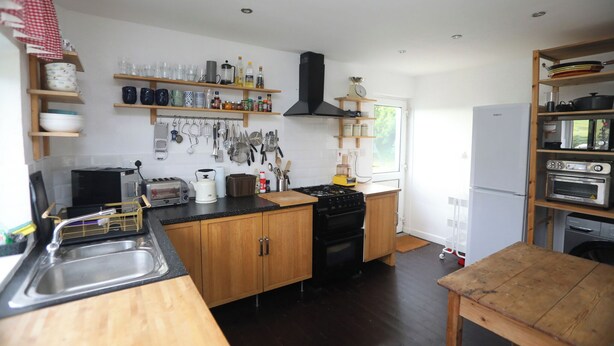 Een kleine keuken met houten kastjes, een zwarte kookplaat en verschillende keukengerei aan de muur.