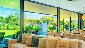 Ein moderner Außenbereich mit einer Sitzecke, Sofas, Stühlen und einem Esstisch, mit Blick auf einen üppigen Garten und einen Pool.