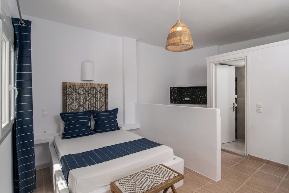 A bedroom with a bed, a bedside table, a hanging light fixture, a door, and a wall with a decorative panel.