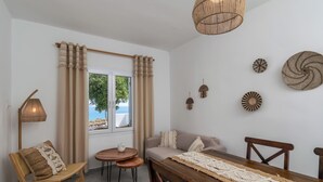 A cozy room with a wooden dining table, a sofa, and a chair. There is a window with curtains, a lamp, and wall decor. - Summer Residence (Milos)