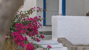 A white building with a blue door, a stone wall, and pink bougainvillea flowers. - Summer Residence (Milos)