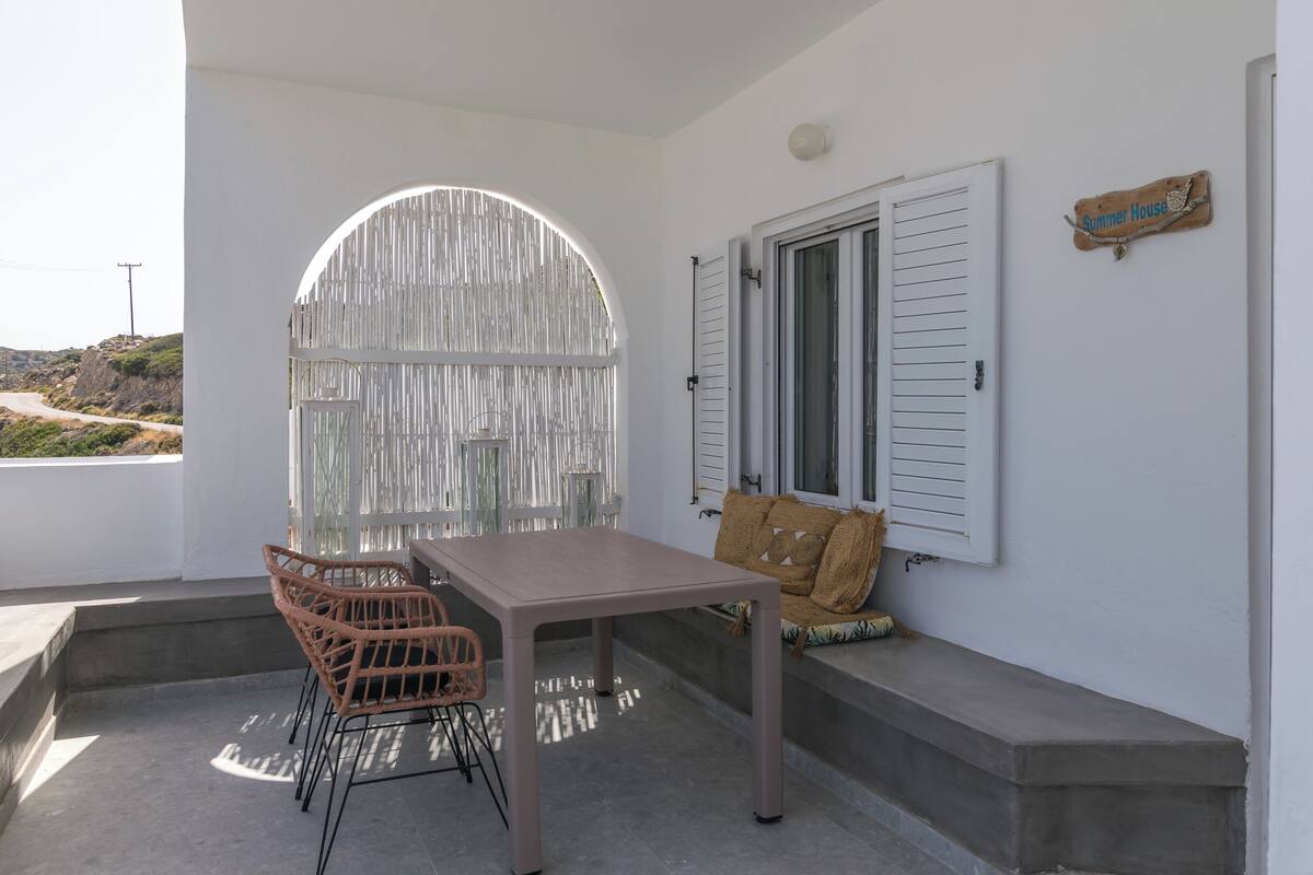 A balcony with a table and chairs, a cushioned bench, a white door, and a sign reading "Summer House".