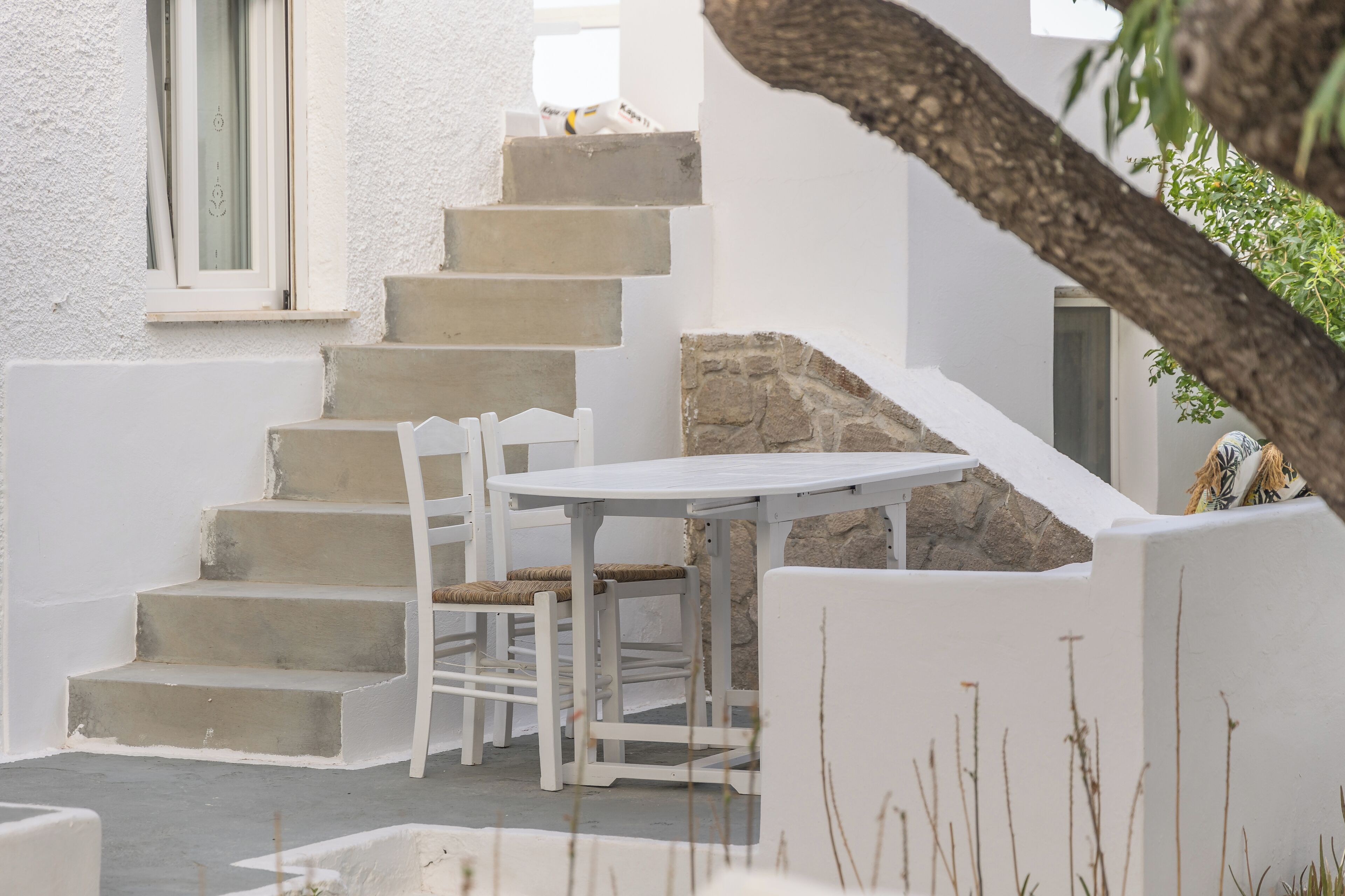Un escalier extérieur blanc menant à un espace de repos abrité, équipé d’une table et de chaises.