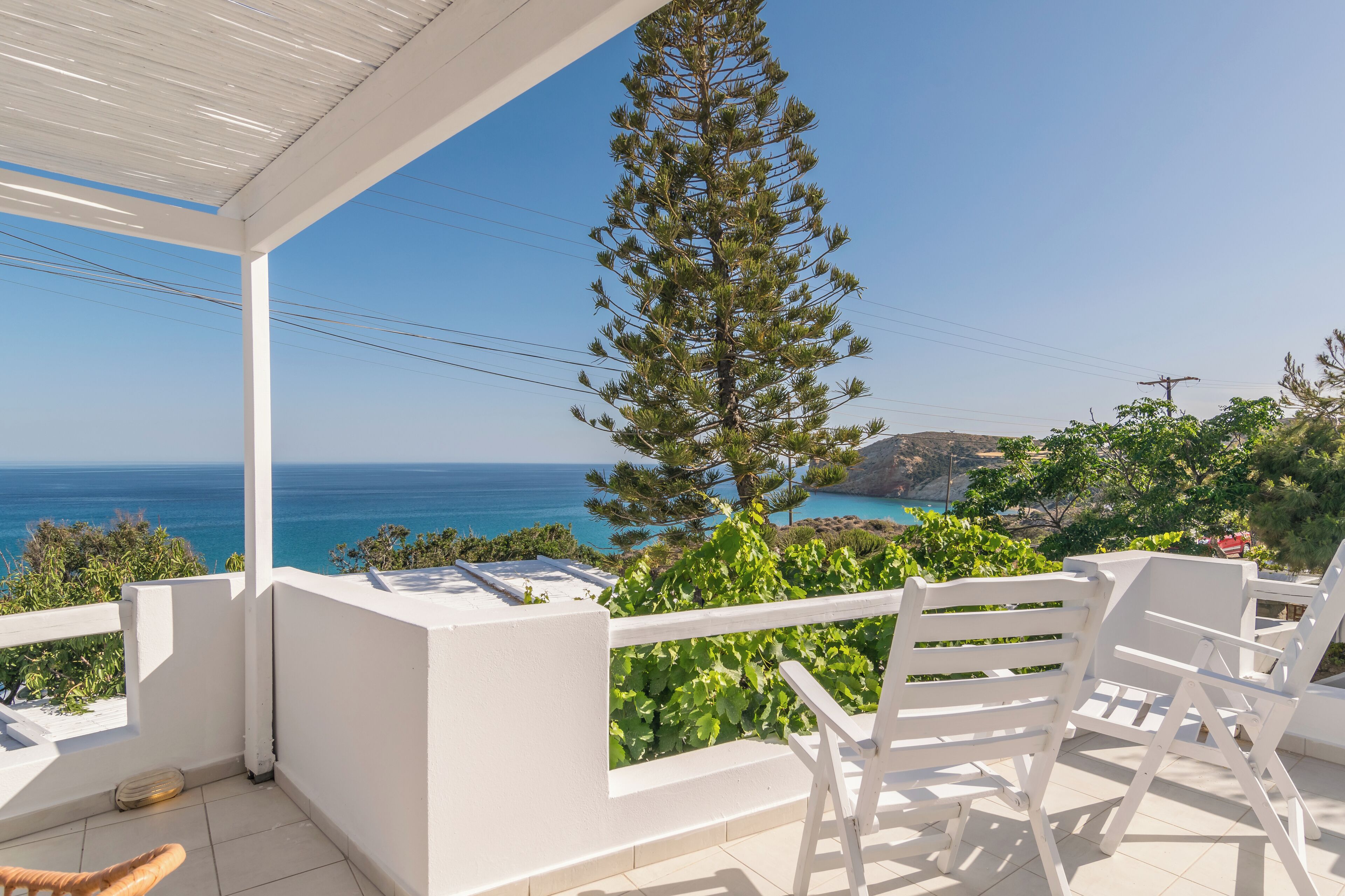 A balcony with white chairs and a view of the sea.