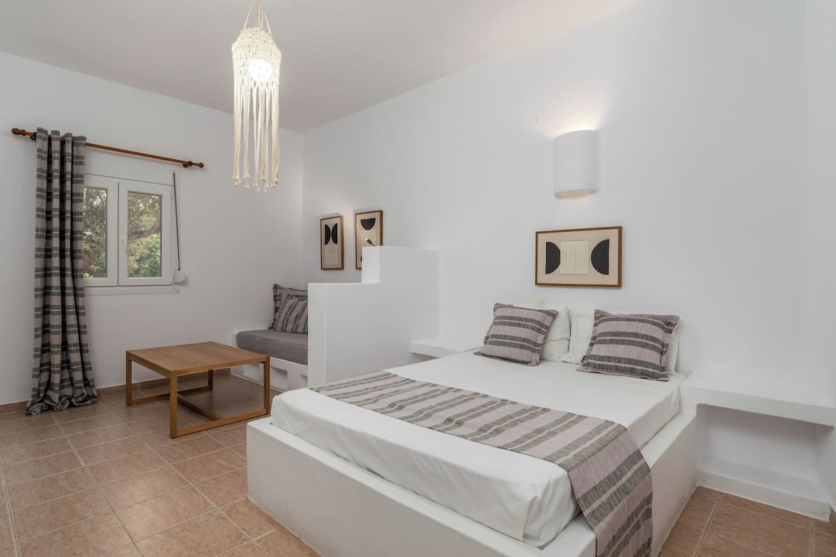 A bedroom with a bed, bedside tables, a hanging light fixture, and a window with curtains.