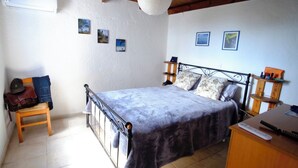 A bedroom with a bed, a wooden chair, a desk, and a nightstand.