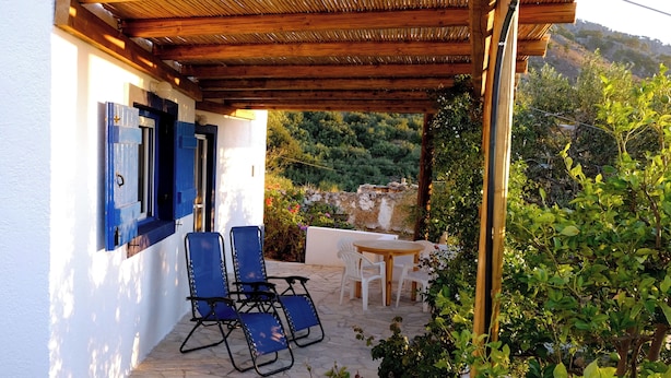 A covered outdoor seating area with stone flooring, blue chairs, and a table.