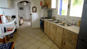 A kitchen with wooden cabinets, a stove, and a sink. There is a window with a view of greenery outside.