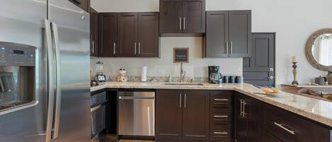 A modern kitchen with dark cabinets, stainless steel appliances, and a granite countertop.