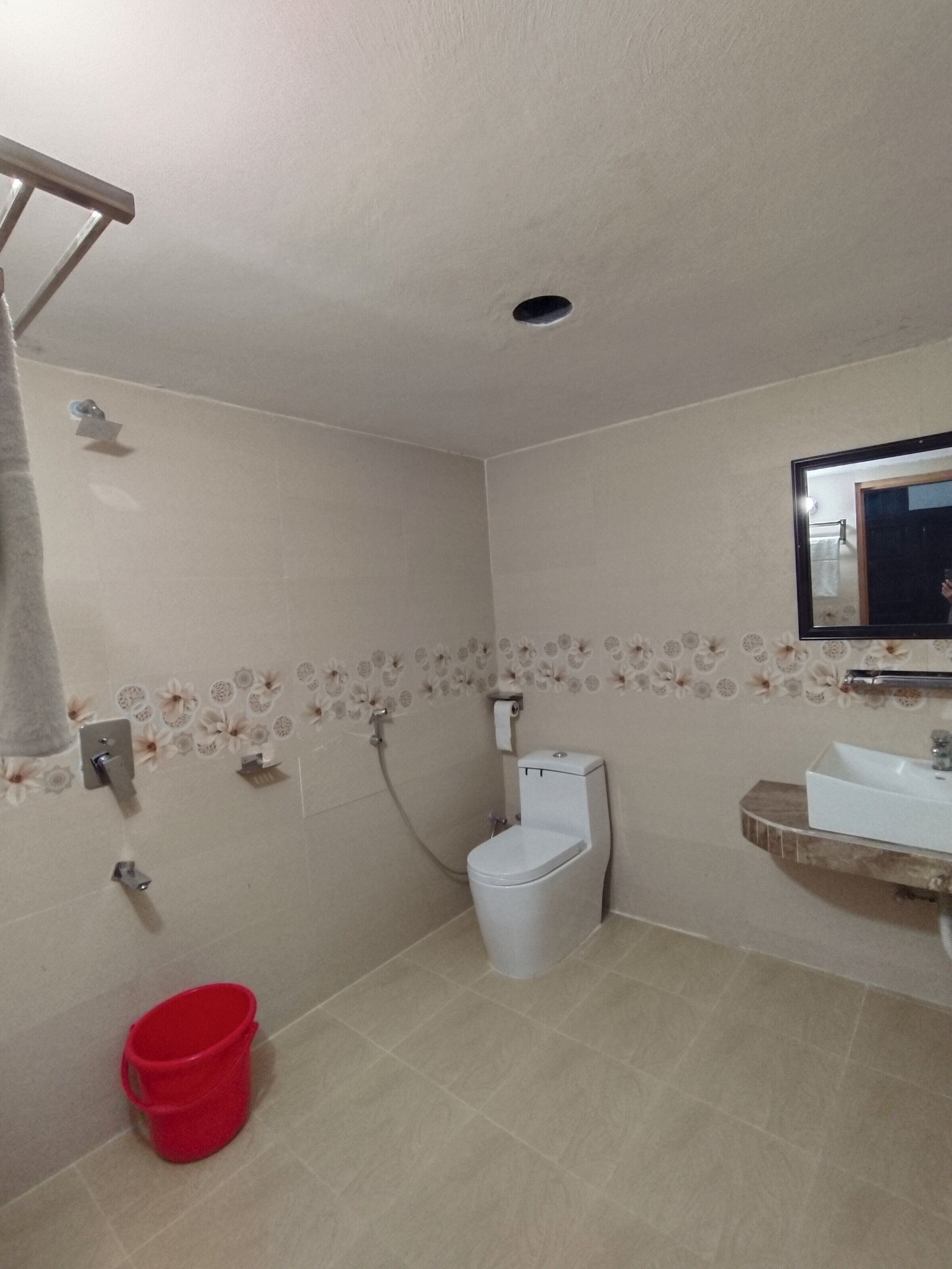 Baño con inodoro, lavabo, ducha y un cubo rojo.