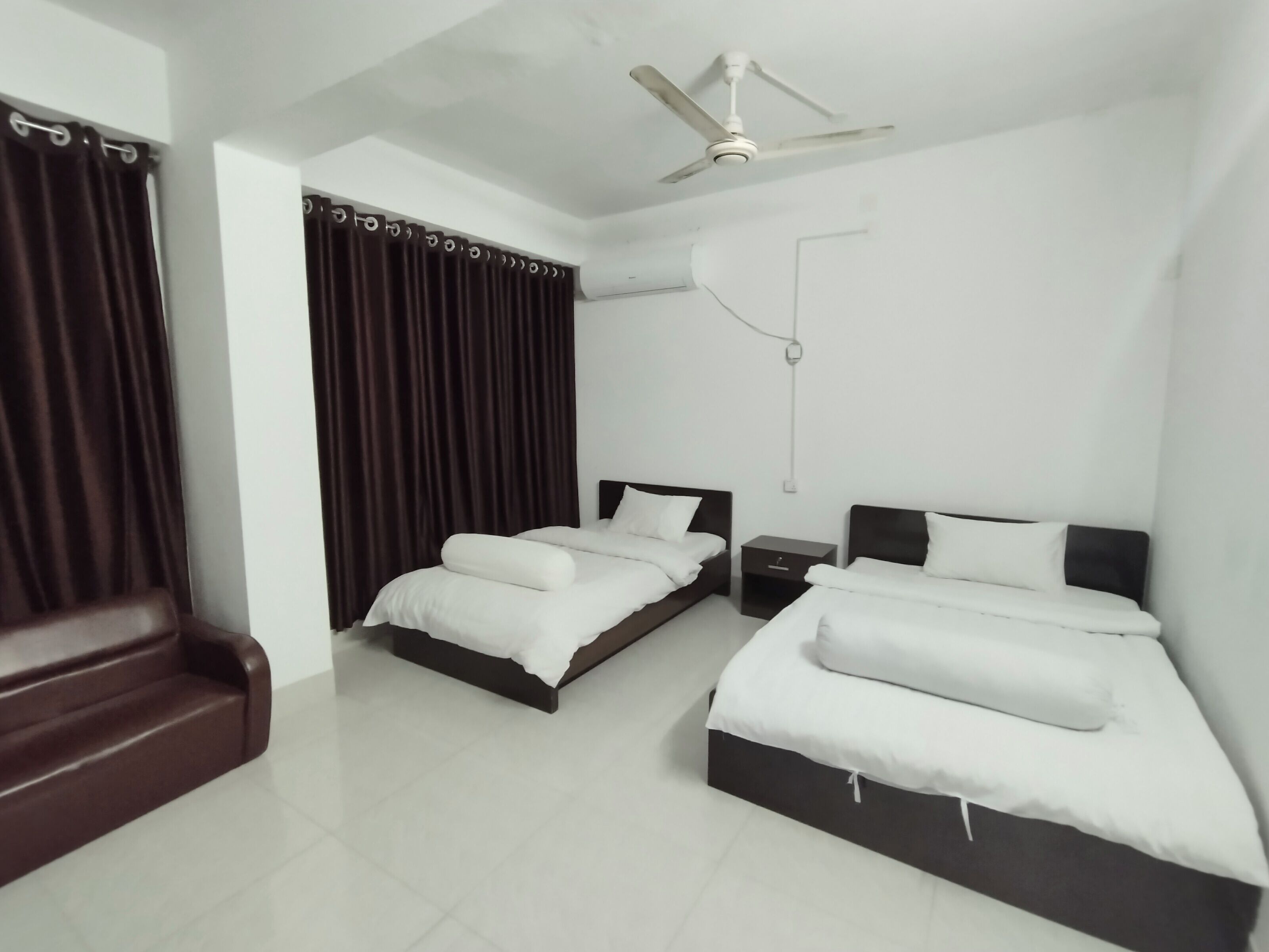 A hotel room with two beds, a ceiling fan, and a window with curtains.