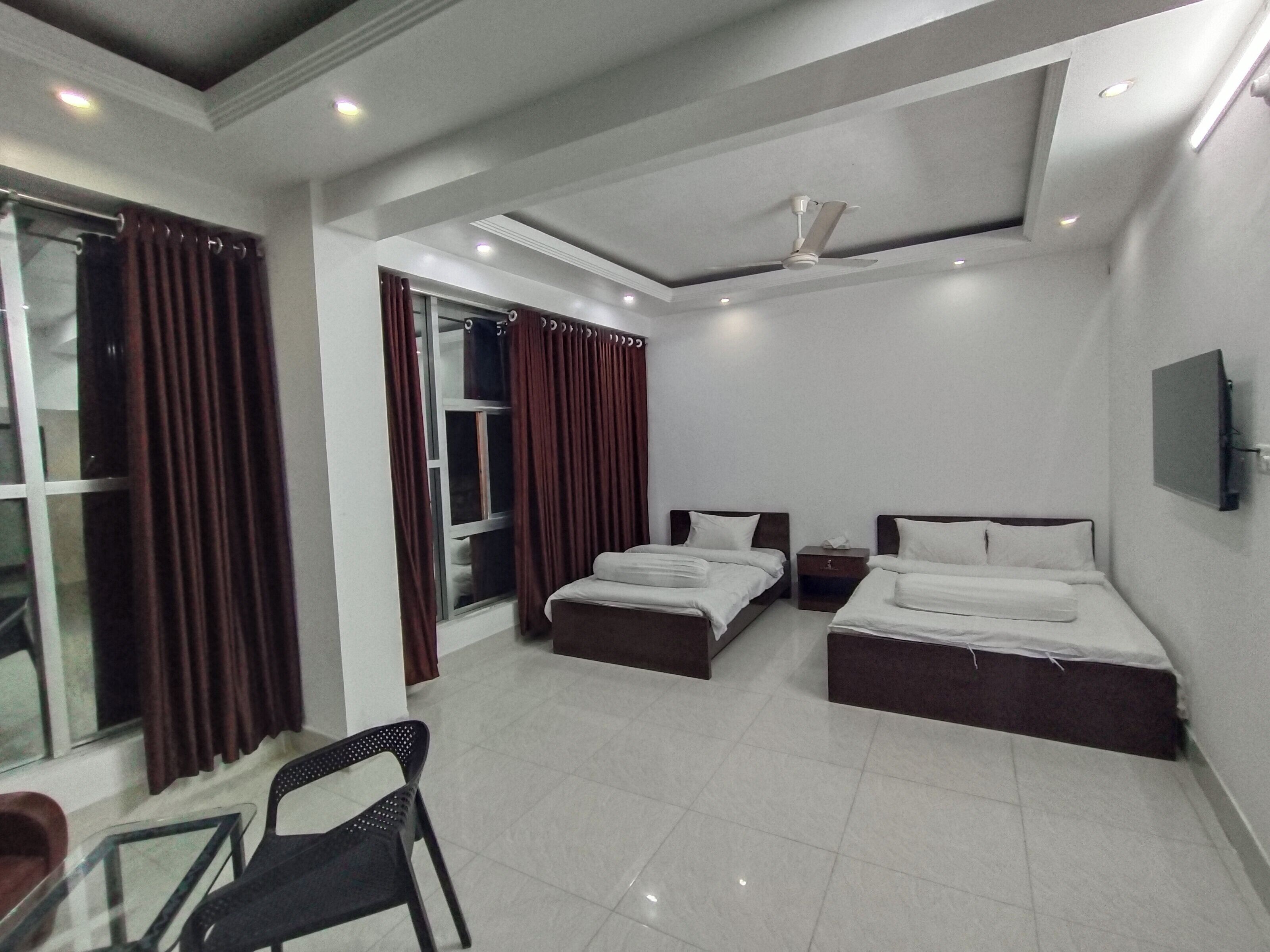 A hotel room with two beds, a TV, a ceiling fan, and a window with curtains.