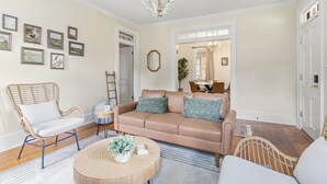 Un soggiorno con un divano color beige, una poltrona in vimini, un tavolino rotondo e un lampadario.