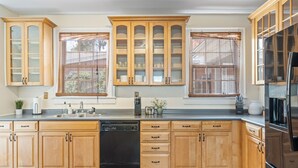 Una cucina con pensili e basi in legno, lavastoviglie, frigorifero e finestra con persiane.