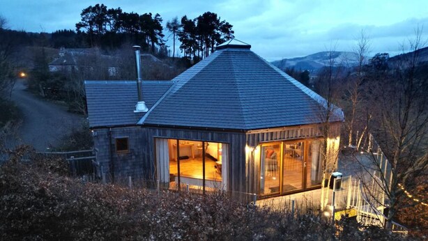 Une maison moderne avec une grande façade vitrée, un toit en pente et une cheminée.