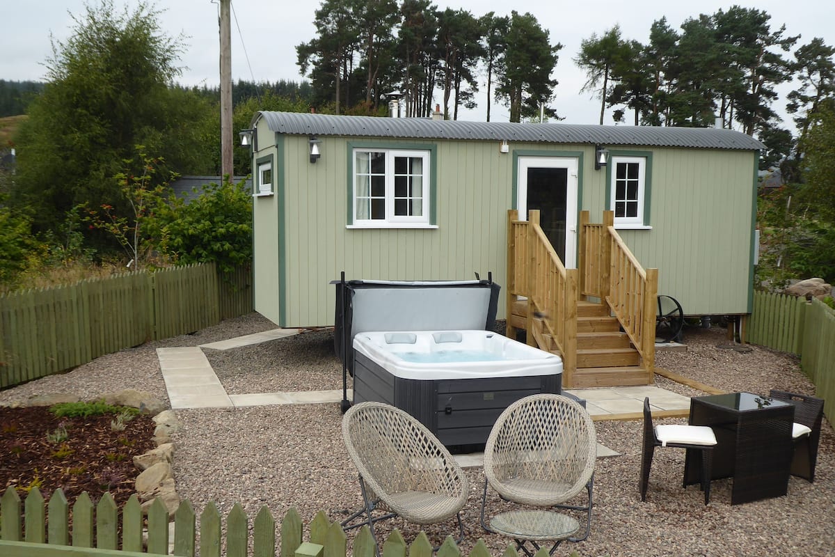 A small, single-story building with a hot tub, two wicker chairs, and a small table.