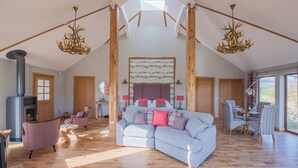 Un loft spacieux avec un plafond haut, des poutres apparentes, un grand canapé d’angle gris agrémenté de coussins rouges et bleus, une cheminée et un coin repas avec des chaises à rayures.