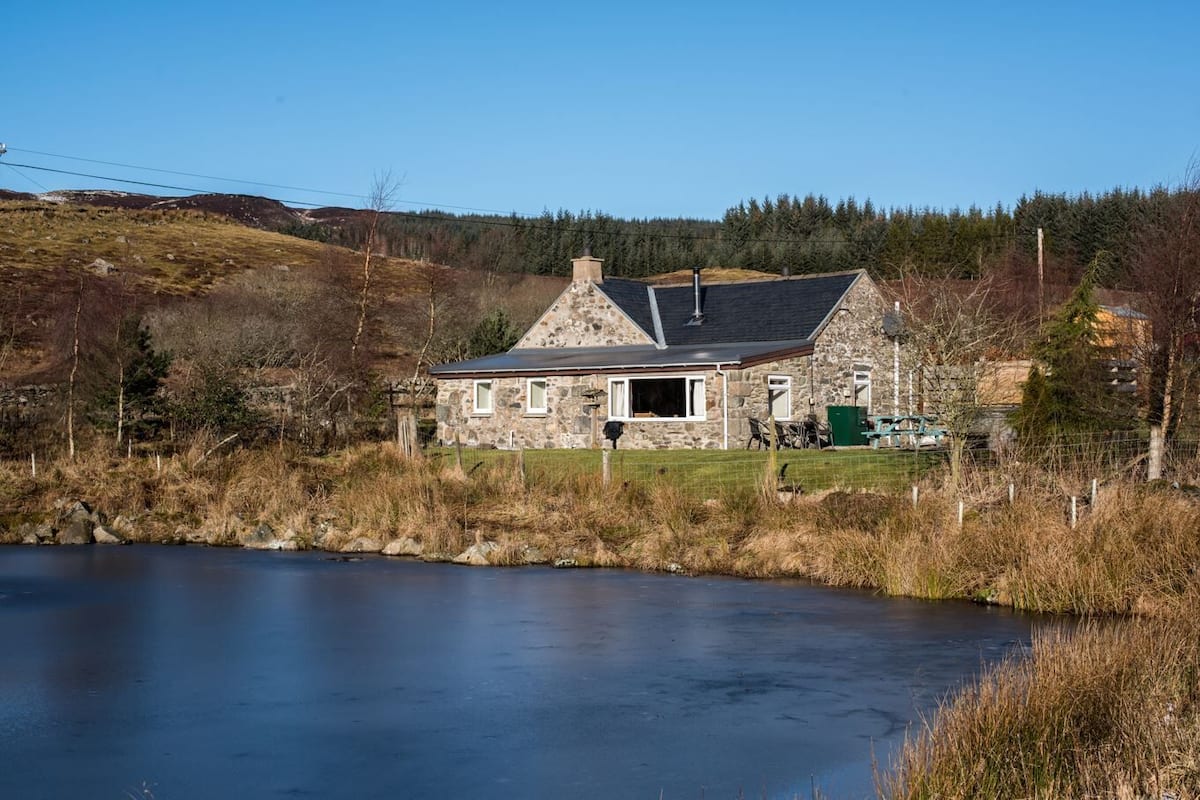 A stone house with a sloped roof, a chimney, and a view of a lake.