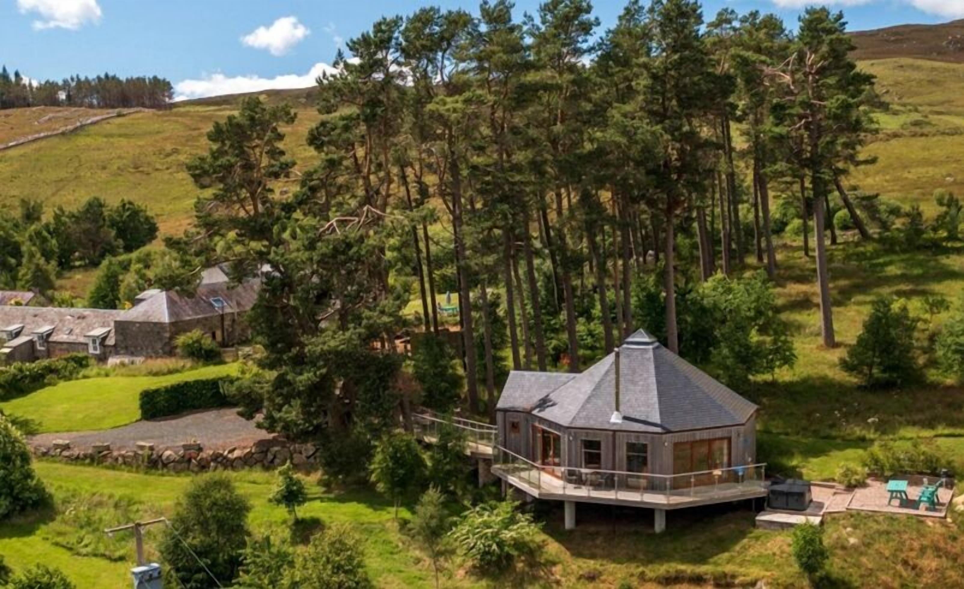 Ein modernes Haus mit einer großen Terrasse, umgeben von Wald und Hügeln.