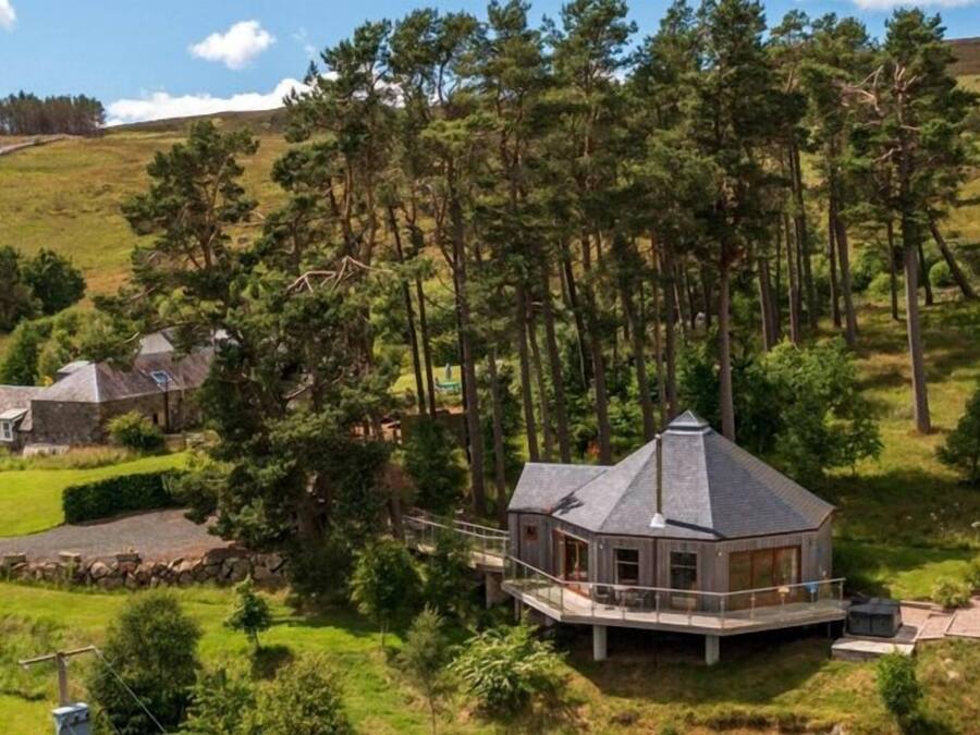 Ein modernes Haus mit einer großen Terrasse, umgeben von Wald und Hügeln.