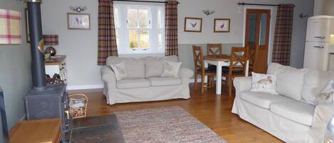 A living room with a sofa, a dining table with chairs, a fireplace, and a window with curtains.
