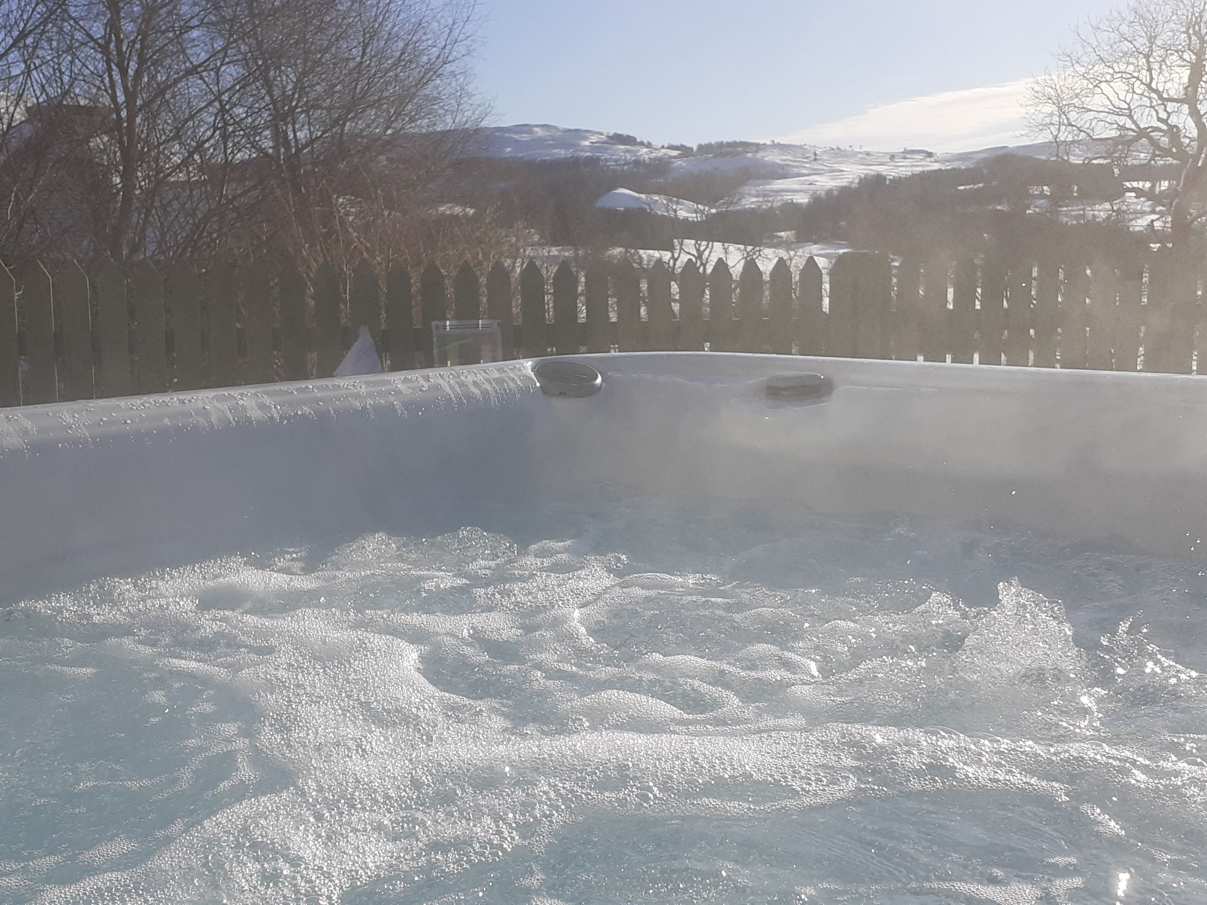 Un jacuzzi con valla de madera y colinas nevadas al fondo.