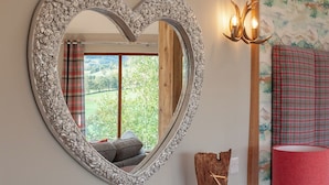 Un miroir en forme de cœur avec un cadre floral, un rideau à carreaux, une lampe rouge et un objet décoratif en bois.
