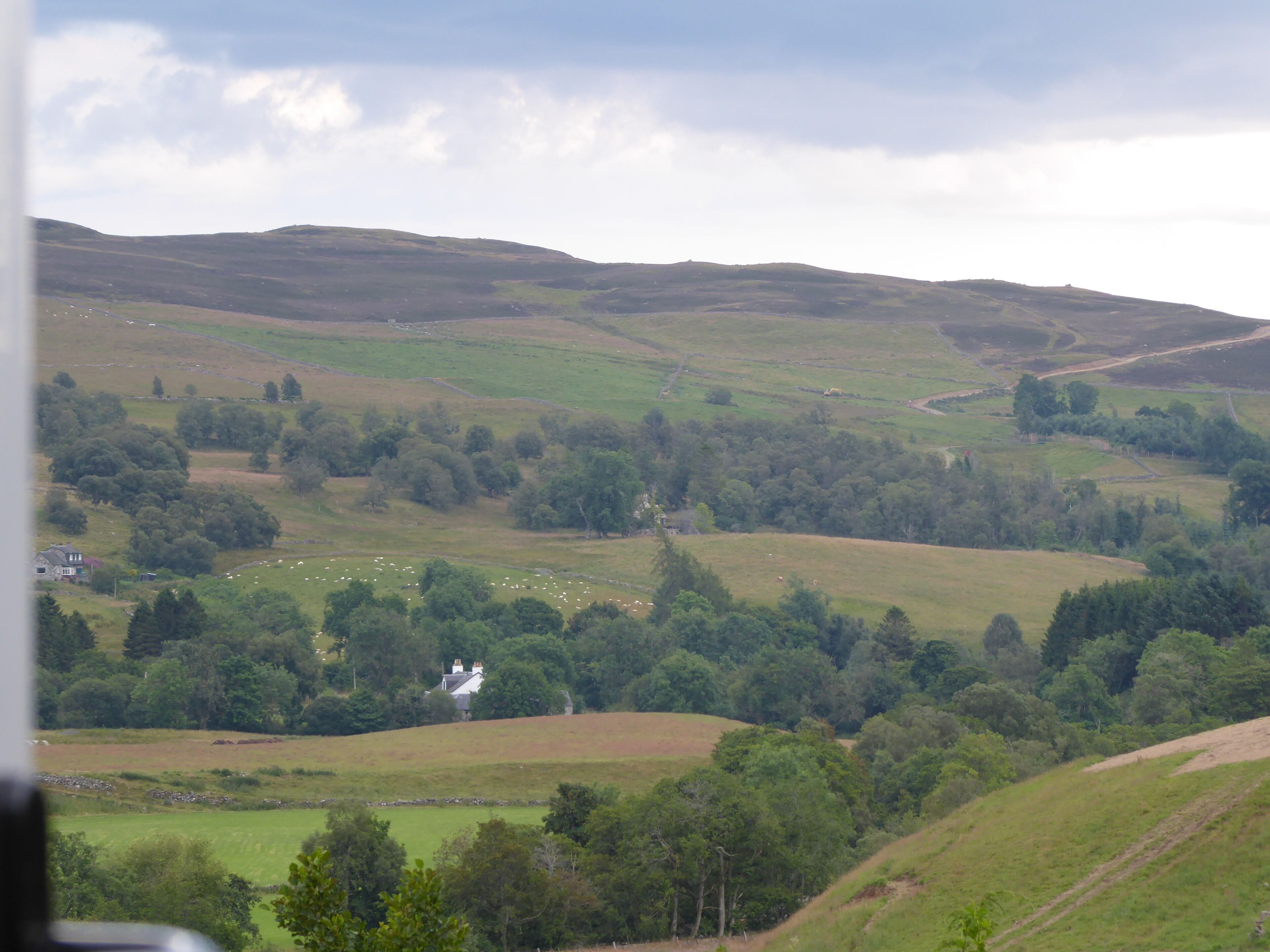 A rural landscape with rolling hills, scattered trees, and a few buildings.