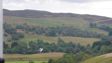 A rural landscape with rolling hills, scattered trees, and a few buildings.