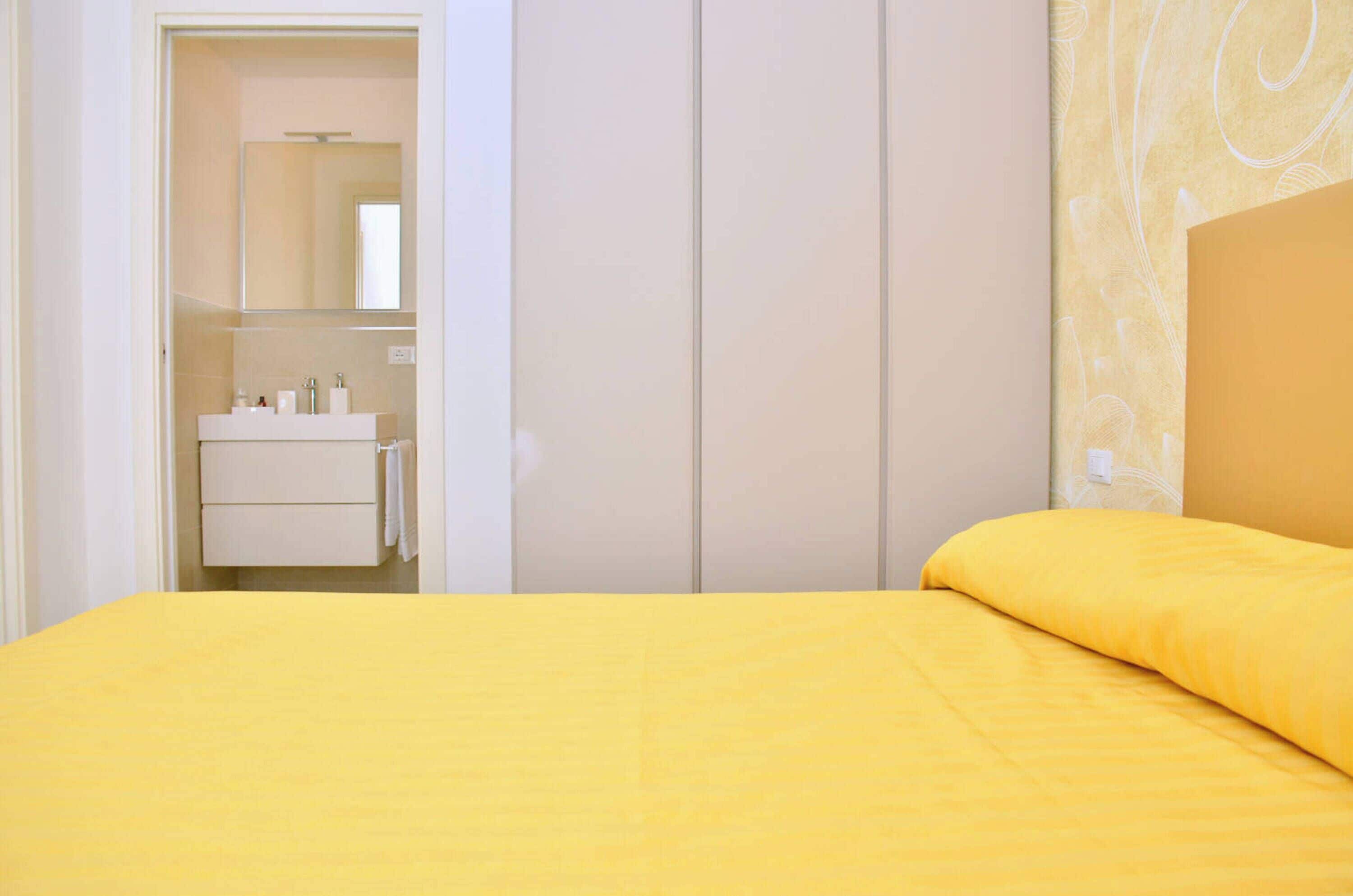 Un dormitorio con cama, armario y baño visible a través de una puerta abierta.