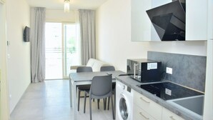 Una cocina moderna con microondas, estufa y lavadora integrados. Cuenta con una zona de comedor con mesa y sillas, y un ventanal con cortinas.