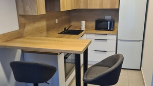 Une cuisine moderne avec des meubles en bois, un plan de travail noir, un four à micro-ondes et un réfrigérateur. On y trouve deux tabourets de bar et un évier avec un robinet.