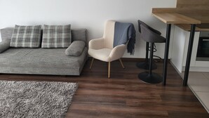 Un salon moderne avec un canapé gris, un fauteuil beige, un tabouret de bar noir et un tapis à poils longs gris.