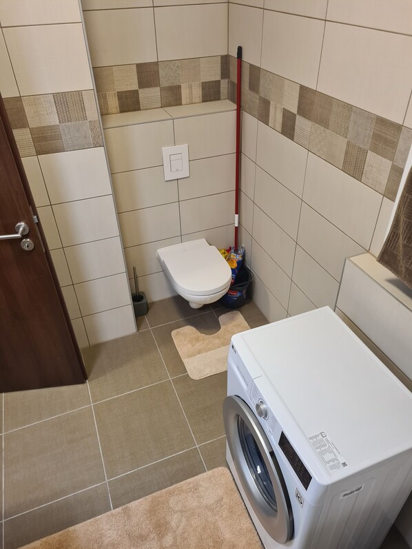 A small bathroom with a toilet, a washing machine, and a mop leaning against the wall.