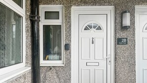 A white door with a small window above it, a doorbell, and a sign reading "2B Ouston Oasis".