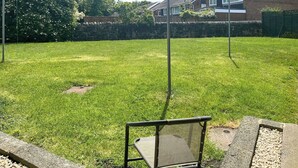 A grassy backyard with a metal chair and a brick wall.