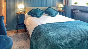 A bedroom with a bed, two bedside tables with lamps, a blue chair, and a floral wallpaper pattern.