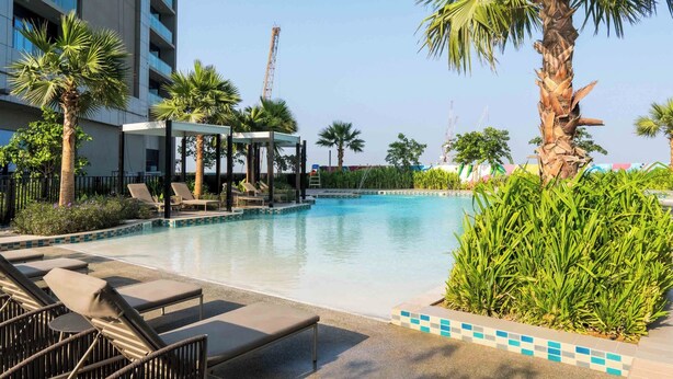 A swimming pool with lounge chairs and palm trees, surrounded by a modern building.