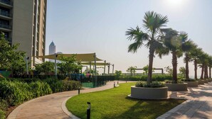 A landscaped pathway with palm trees, a playground, and a building with a distinctive tower in the background.