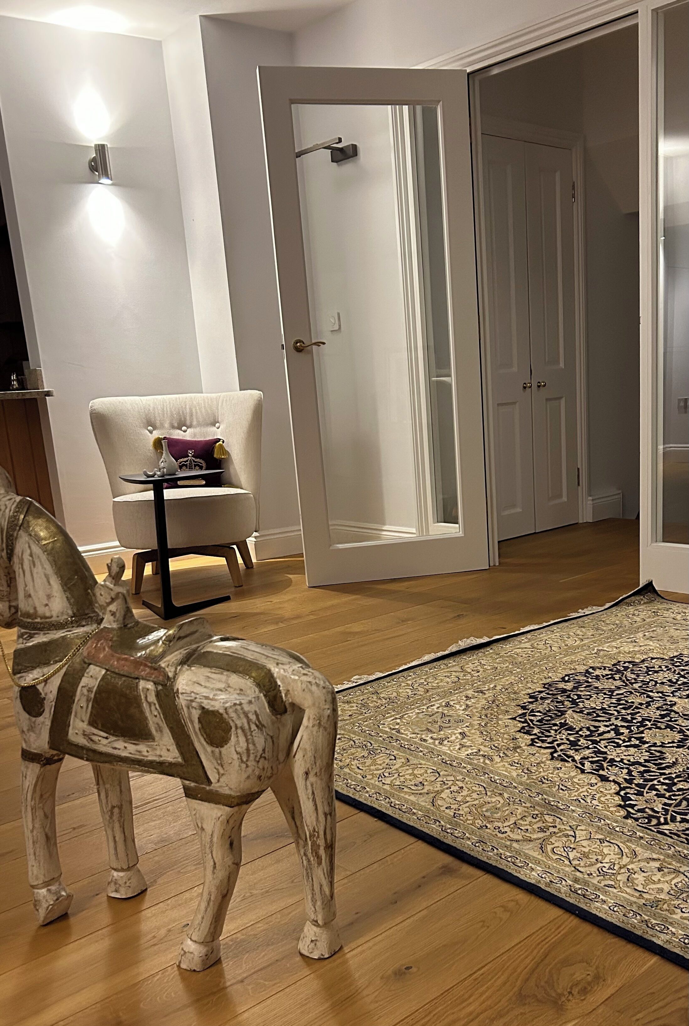 A room with a wooden floor, a white chair with a cushion, a decorative horse statue, and a patterned rug.