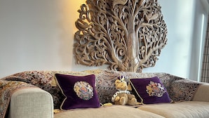 A living room with a beige sofa, patterned cushions, a decorative tree wall art, and a patterned rug. - Windsor Castle panoramic views. Stay in the heart of Royal history (Eton)