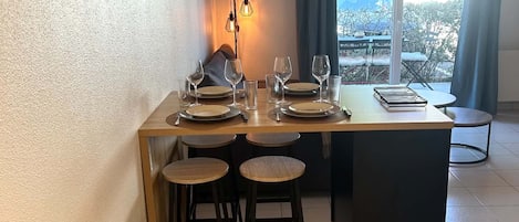 Ruokailutila, jossa on neljälle katettu ruokapöytä, baarijakkar ja ikkunasta avautuva näkymä ulos.