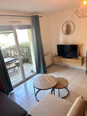 A living room with a TV, a sofa, a coffee table, and a sliding glass door leading to an outdoor area.