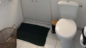 Een badkamer met een wit wastafelmeubel, een spiegel, een toilet en een zwarte badmat.
