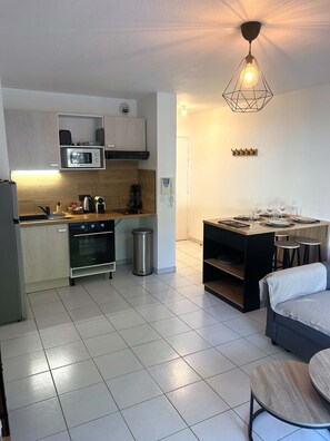 A compact kitchen with a microwave, oven, and a hanging light fixture. - Apartment Pessac- Ideal location (pessac)