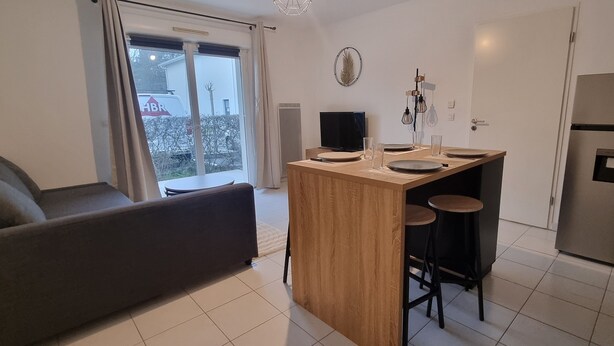 A modern kitchen with a central island, bar stools, a refrigerator, and a dining area with a sofa and table.