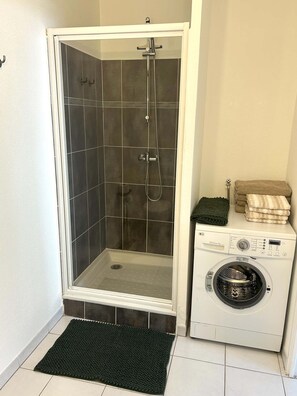 A shower enclosure with a white frame, a washing machine, and a mat.