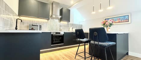 A modern kitchen with dark cabinetry, a central island with bar stools, and a dining area.